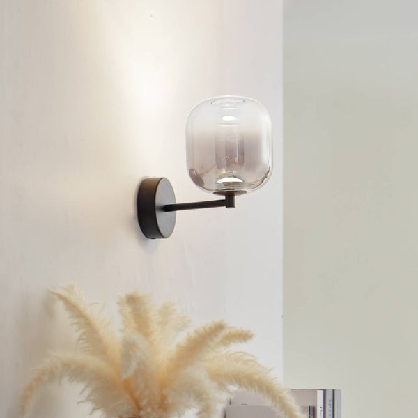 Moderne Wandleuchte mit abgerundetem Glasschirm und schwarzer Metallhalterung, an einer Wand montiert und beleuchtet.