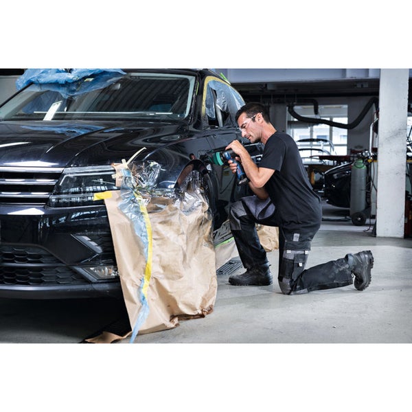 Ein Mann repariert mit einem Akkuschrauber ein Auto in einer Werkstatt.