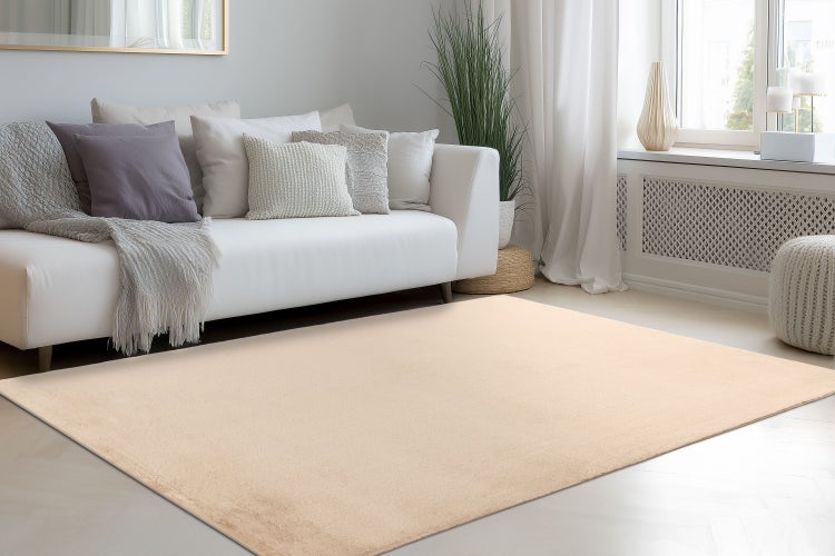 Ein unifarbener Teppich vor einem Sofa in einem hell eingerichteten Wohnzimmer.