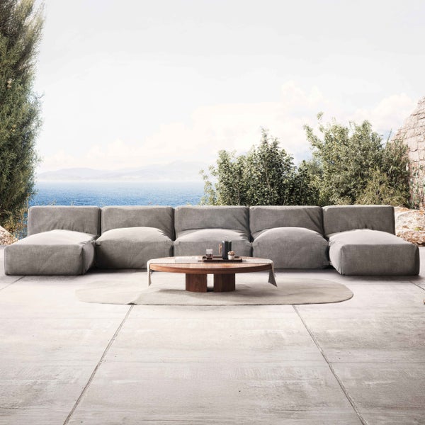 Modulares Garten-Lounge-Sofa aus grauem Stoff mit Holzcouchtisch auf einer modernen Terrasse mit Meerblick und Steinplatten.