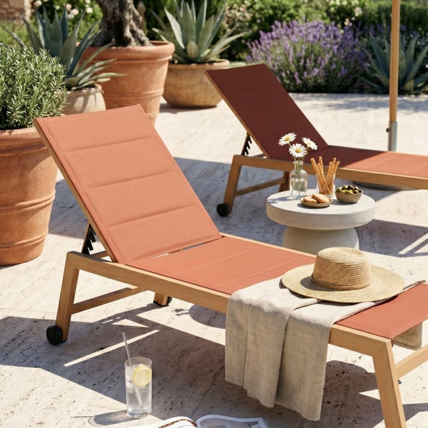 Sonnenliege aus Holz mit terracottafarbenem Bezug auf einer hellen Steinterrasse mit Pflanzen und Beistelltisch in mediterraner Atmosphäre.