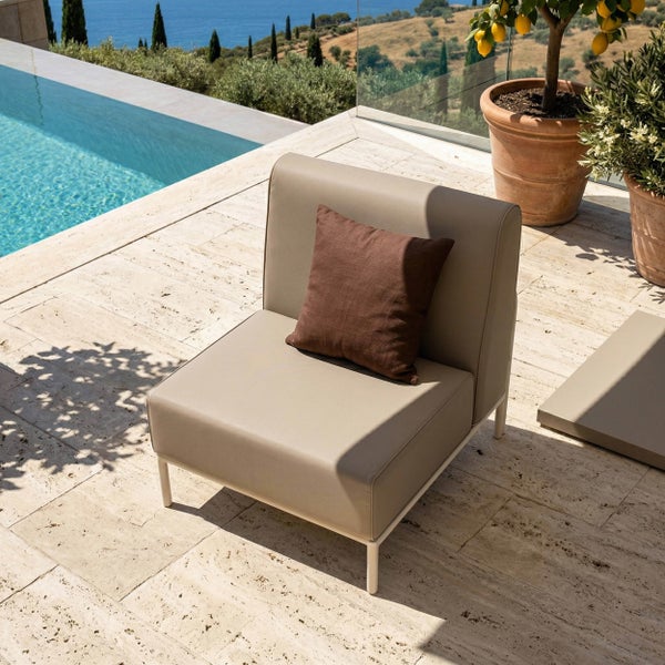 Moderner Outdoor Loungesessel mit braunem Kissen auf einer hellen Steinterrasse neben einem Pool mit Aussicht auf eine mediterrane Landschaft.