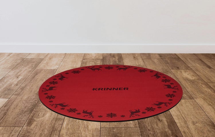 Runde rote Christbaumunterlage mit Krinner Logo und Muster aus Rentieren und Schneeflocken auf einem hellen Holzboden.