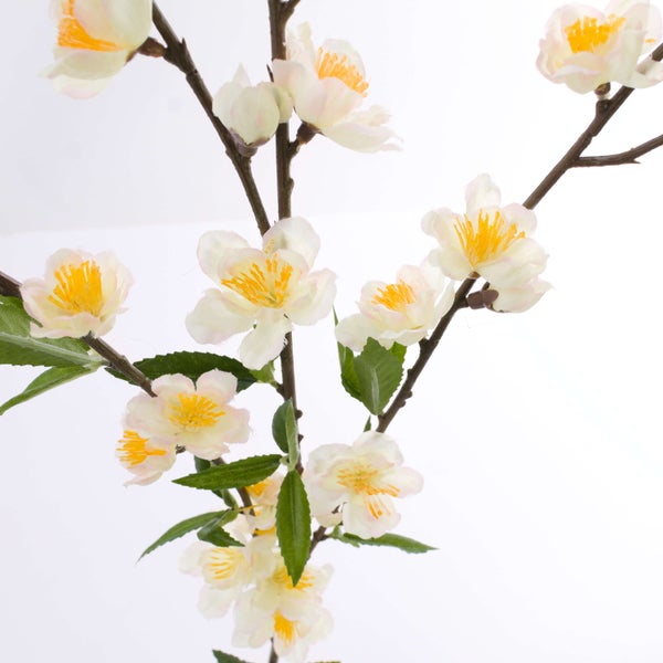 Künstlicher Blütenzweig mit weißen Blüten, gelben Staubblättern und grünen Blättern an braunem Stiel.