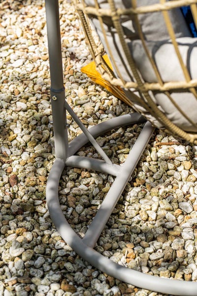 Detailansicht des Metallgestells eines Hängesessels auf Kiesboden mit einem Korb aus Kunststoffgeflecht und Polstern.