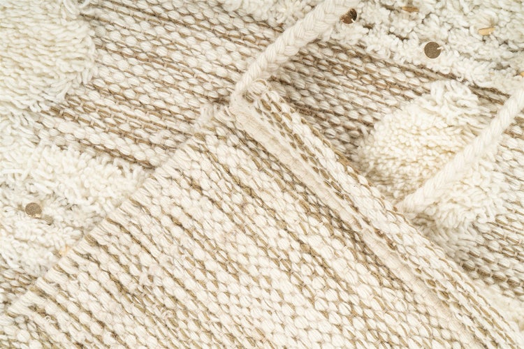 Nahaufnahme eines gewebten Teppichs mit strukturierten Mustern, getufteten Details und kleinen metallischen Akzenten.