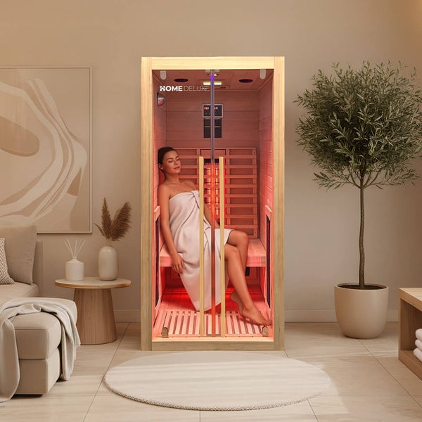 Eine Person sitzt in einer Home Deluxe Infrarotkabine aus Holz im Wohnzimmer, entspannt und in ein Handtuch gehüllt.