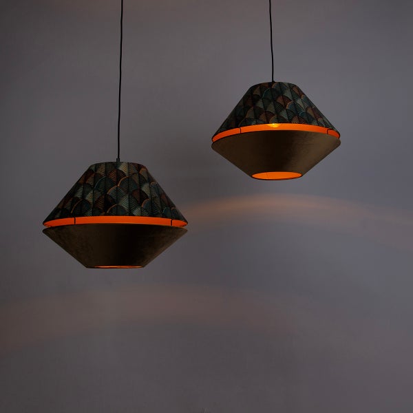 Zwei eingeschaltete Pendelleuchten mit bikonischem Schirm, oben gemusterter Stoff, unten dunkler Samt, strahlen warmes Licht aus.
