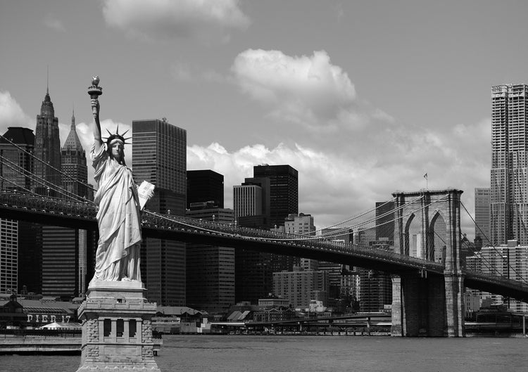 Schwarzweißaufnahme der Freiheitsstatue und der Brooklyn Bridge vor der Skyline von New York.