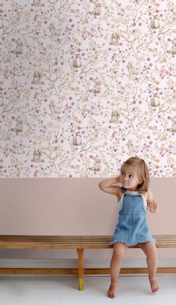 Zimmer mit Tapete mit Blumen- und Hasenmuster, auf einer Bank sitzt ein kleines Mädchen.
