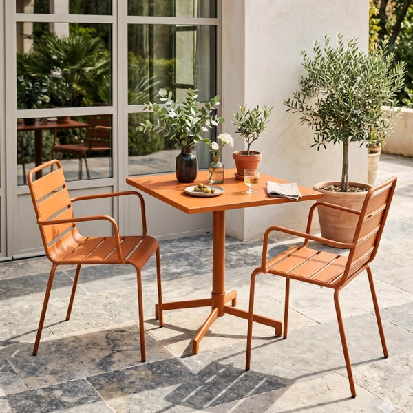 Modernes Bistro-Set für den Außenbereich mit quadratischem Metalltisch und zwei Armlehnenstühlen auf einer hellen Steinterrasse mit Pflanzen.