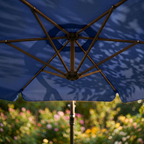 Unteransicht eines Sonnenschirms mit blauem Bezug und braunem Metallgestell im Garten.