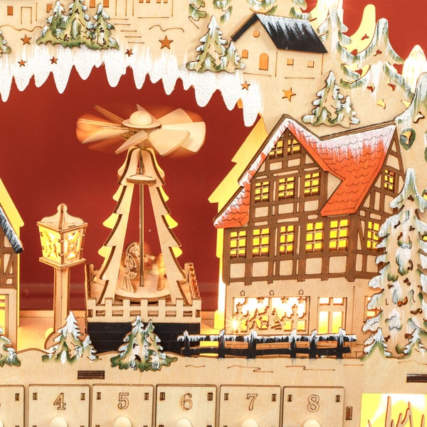 Detailansicht eines beleuchteten Adventskalenders aus Holz mit Winterdorf-Motiv, Fachwerkhäusern und einer kleinen Weihnachtspyramide.
