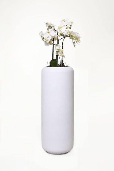 Künstliche Orchidee in einem hohen, weißen zylindrischen Pflanzgefäß.