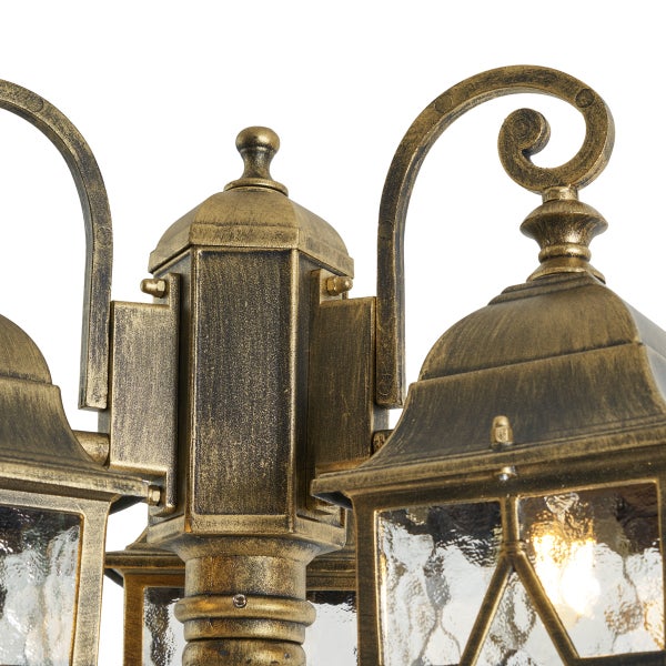 Detail einer dreiflammigen Außenleuchte in antik goldfarbenem Design mit Schnörkeln und strukturiertem Glas.