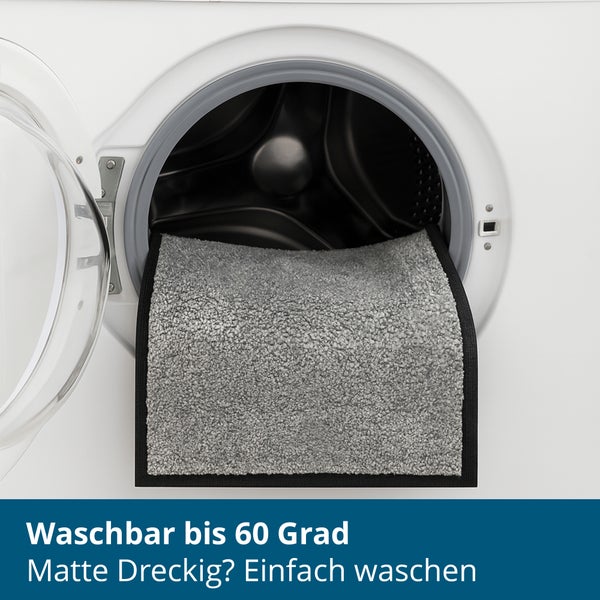 Eine Fußmatte liegt zur Reinigung in der offenen Trommel einer Waschmaschine, die bis 60 Grad waschbar ist.