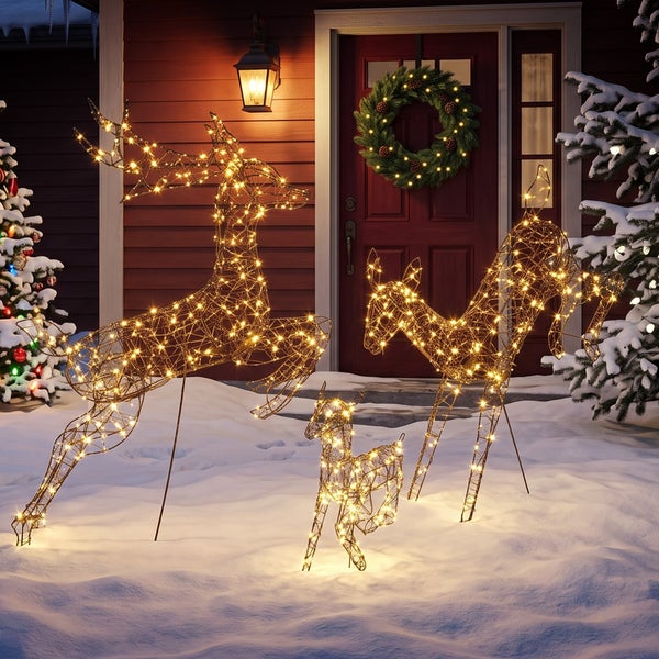 Weihnachtsdekoration mit leuchtenden Rentierfiguren aus Metalldraht vor einem Haus mit Schnee und Tannenbaum.