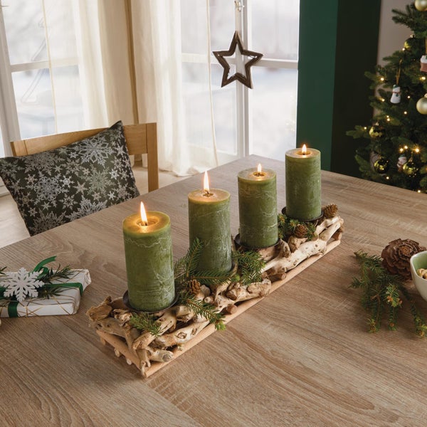 Vier brennende Stumpenkerzen in gruen auf einem rustikalen Treibholz Kerzenhalter als weihnachtliche Tischdekoration auf einem Holztisch.