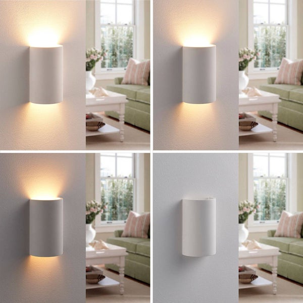 Weiße zylindrische Wandleuchte mit Up-and-Down-Lichteffekt in einem hellen Wohnzimmer mit grünem Sofa und Fenster.