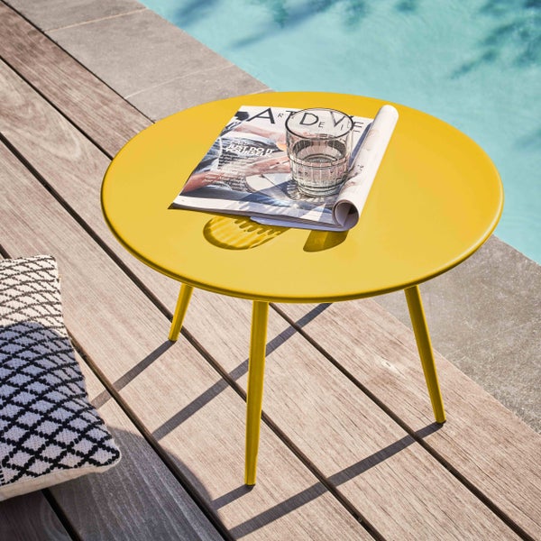 Runder gelber Beistelltisch aus Metall auf einer Holzterrasse neben einem Pool.