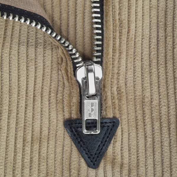 Detailansicht eines Metallreißverschlusses auf Cordstoff mit Job Logo am Schieber und einer Lederverstärkung.