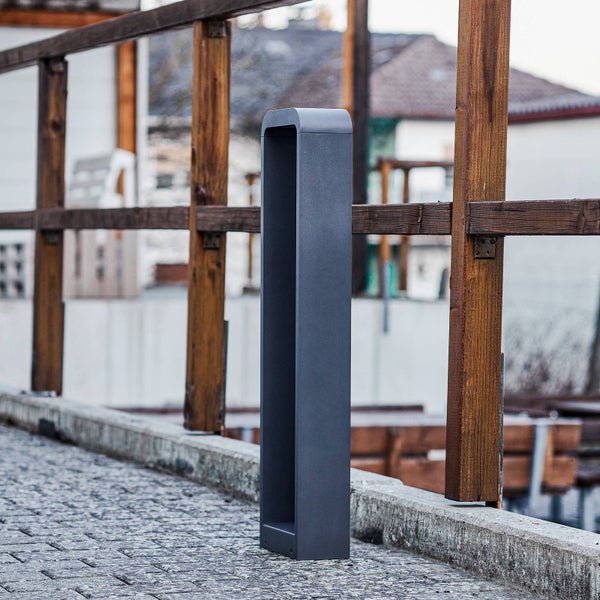 Rechteckige Außenwegeleuchte in Anthrazit mit hohlem Rahmen, montiert auf einem gepflasterten Weg neben einem Holzgeländer im Freien.