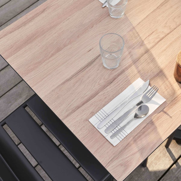 Gartentisch mit hellbrauner Tischplatte in Holzoptik, Gläsern und Besteck auf einer Terrasse mit schwarzen Gartenstühlen.