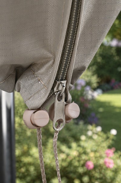 Detailaufnahme eines Reißverschlusses und eines Kordelzugs mit Stoppern an einer beigefarbenen Schutzhülle.