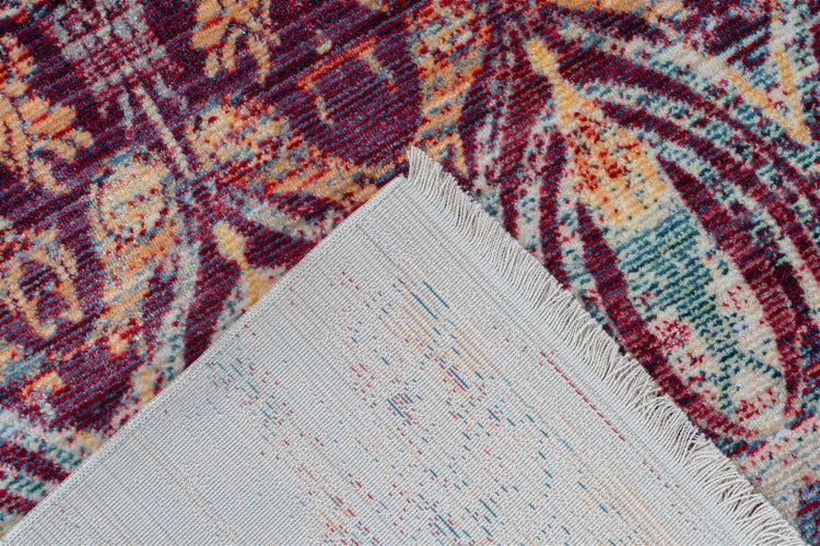 Nahaufnahme eines Teppichs mit buntem Vintage-Blumenmuster und umgeschlagener Ecke, die die helle Unterseite und Fransen zeigt.