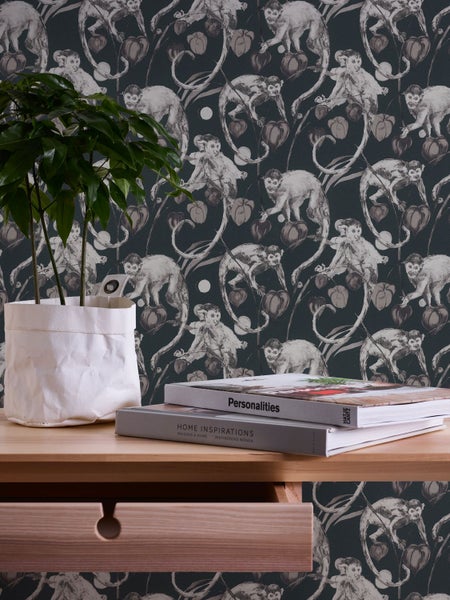Nahaufnahme einer Wand mit einer Tapete mit einem Affenmuster, einem Holztisch mit einer Pflanze und zwei Büchern