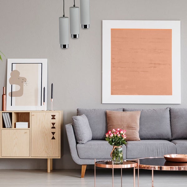Modernes Wohnzimmer mit grauem Sofa, Sideboard aus Holz, drei zylindrischen Pendelleuchten und gerahmten Kunstwerken in hellem, organisiertem Stil.