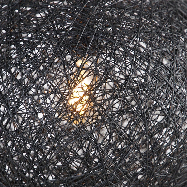 Detailansicht eines runden Lampenschirms aus verflochtenen dunklen Fasern mit einer leuchtenden Glühbirne im Inneren.