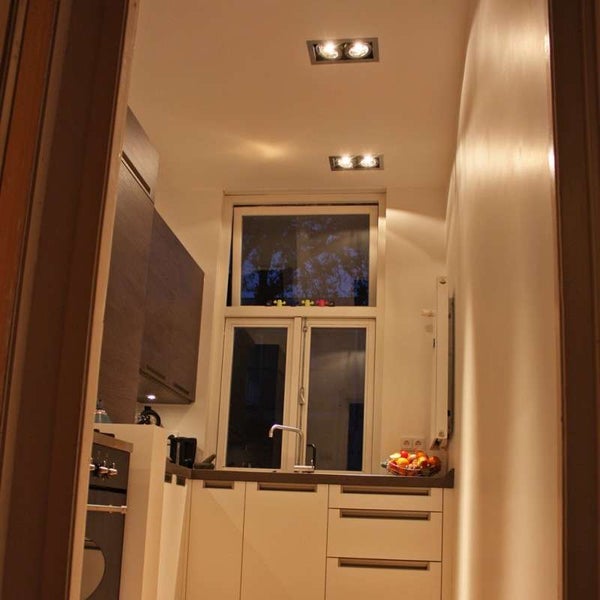 Moderne kleine Küche mit hellen Unterschränken, dunklen Hängeschränken aus Holz, Spülbecken unter dem Fenster und Deckeneinbaustrahlern.