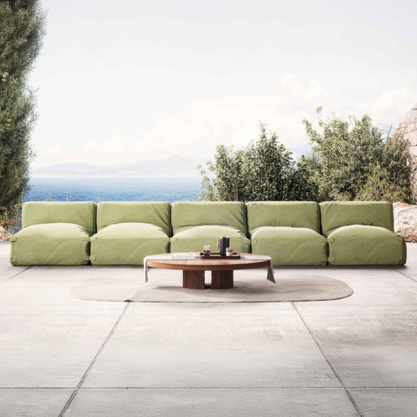 Fünfteiliges modulares Outdoor-Lounge-Sofa in Hellgrün mit ovalem Holz-Couchtisch auf einer hellen Steinterrasse mit weitem Meerblick.