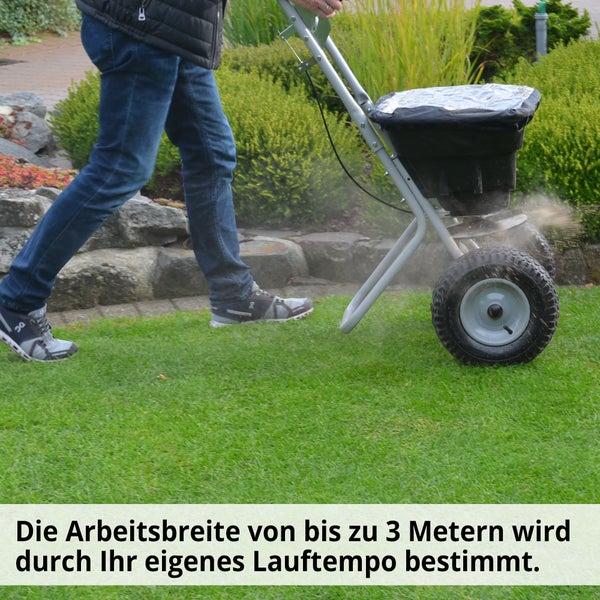 Person schiebt einen Streuwagen auf einer Rasenfläche.