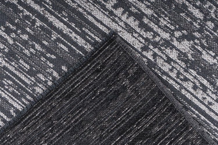 Detailaufnahme eines grau gemusterten, gewebten Teppichs mit strukturierter Rückseite an einer umgeschlagenen Ecke.