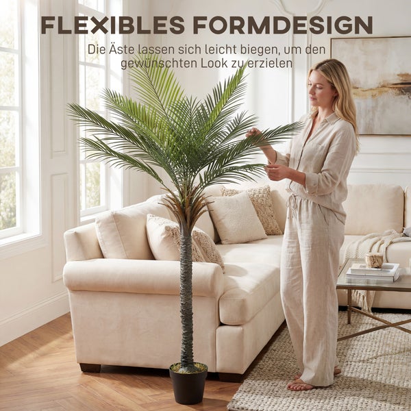 Eine Frau richtet die flexiblen Äste einer künstlichen Palme in einem hellen Wohnzimmer aus.