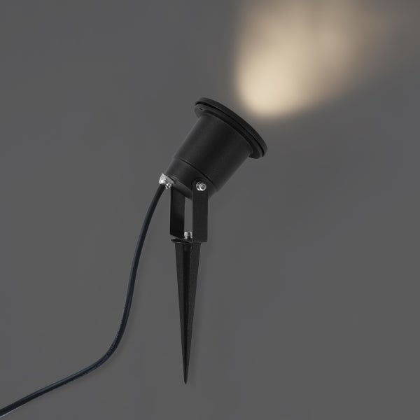 Schwarzer Gartenstrahler mit Erdspieß und Kabel, strahlt warmweißes Licht aus.