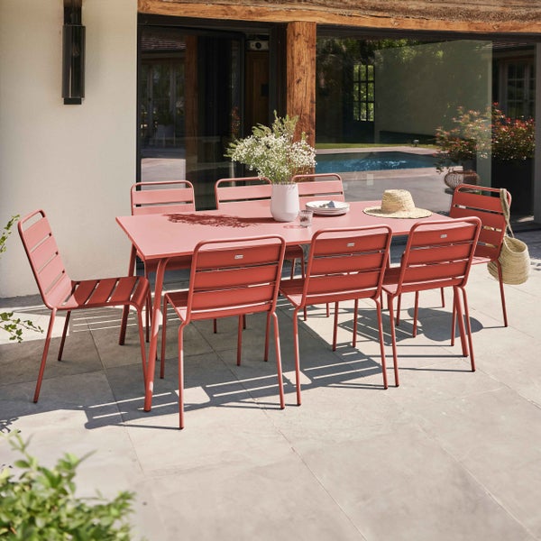 Modernes Gartenmöbel-Set aus Metall auf einer Terrasse mit Pool. Ein rechteckiger Tisch mit acht Lamellenstühlen, dekoriert mit Vasen und Geschirr.