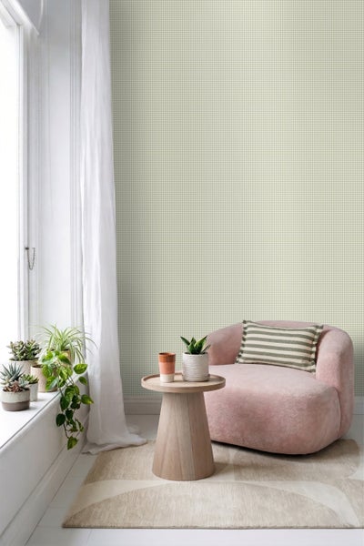 Vliestapete mit feinem Karomuster in einem hellen Wohnzimmer mit rosa Sessel, Holzbeistelltisch und Zimmerpflanzen am Fenster.