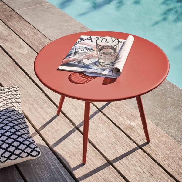 Runder roter Gartenbeistelltisch aus Metall auf einer Holzterrasse am Pool mit einer Zeitschrift und einem Glas.