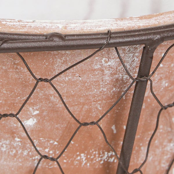 Detail eines Terrakotta-Pflanztopfes mit einem braunen Drahtgeflecht und patinierter Oberfläche.