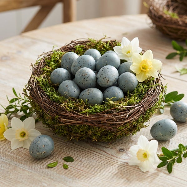 Osternest mit gesprenkelten Eiern auf einem Holztisch dekoriert mit Narzissen und Buchsbaumzweigen als Tischdekoration