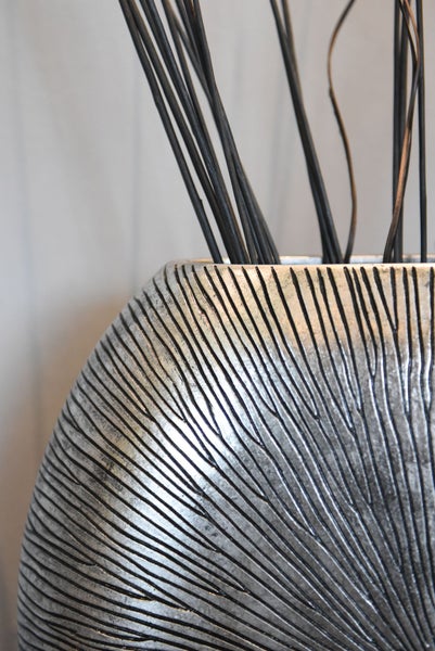 Nahaufnahme einer silbernen Vase mit Rillenstruktur und schwarzen dekorativen Zweigen.