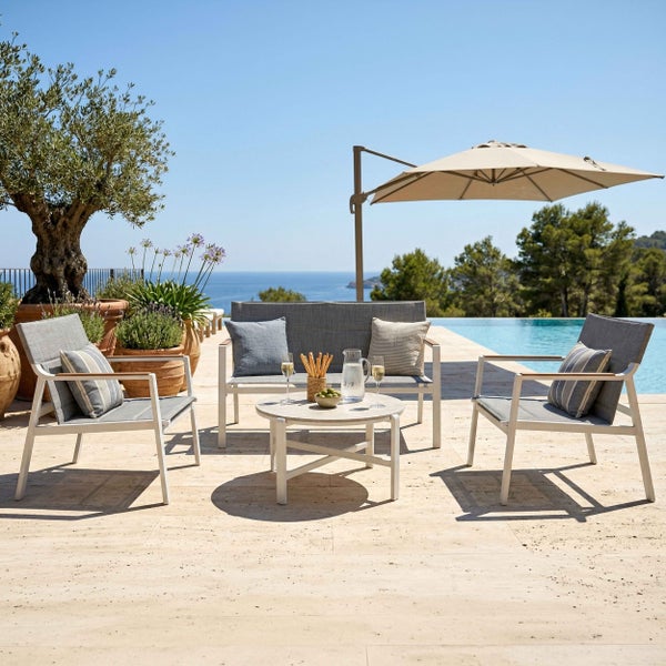 Moderne Lounge-Garnitur aus Metall mit Sofa, zwei Sesseln, rundem Tisch und Ampelschirm auf einer hellen Terrasse am Pool mit Meerblick.