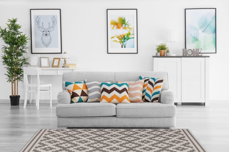 Modernes Wohnzimmer mit hellem Sofa, gemusterten Dekokissen, Teppich mit geometrischem Muster, Kunst an der Wand und Zimmerpflanze.