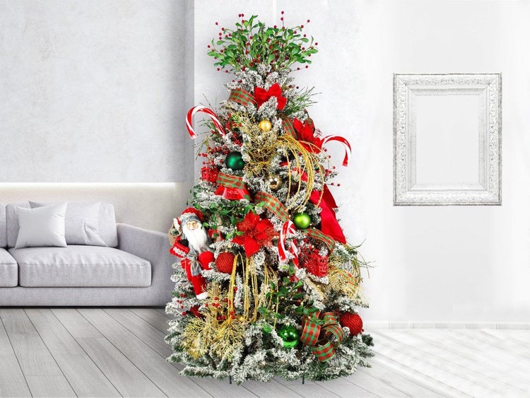 Festlich geschmückter, künstlicher Weihnachtsbaum mit Kunstschnee, Weihnachtsfiguren, Schleifen und Kugeln in einem Wohnzimmer.