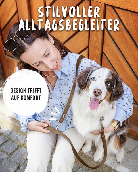Eine Frau sitzt mit einem Hund vor einer Holztür und nutzt eine braune Hundeleine zum Umhängen.