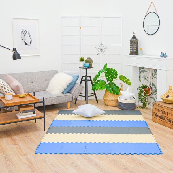 Helles Wohnzimmer mit grauem Sofa, Holztisch und gestreifter Schaumstoffmatte auf Laminatboden. Im Hintergrund Raumteiler und Dekokamin.