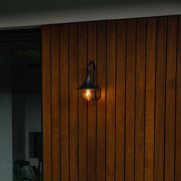 Schwarze Außenwandleuchte aus Metall mit warmem Licht, montiert an einer vertikalen Holzfassade.